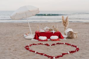 marriage proposal with a picnic and petals in the beach - Photo via Weddings and Events by Natalia Ortiz