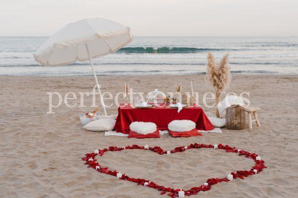 marriage proposal with a picnic and petals in the beach - Photo via Weddings and Events by Natalia Ortiz